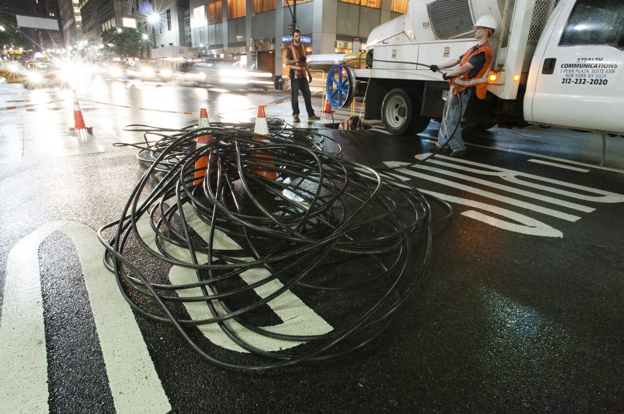 Crew installing fiber-optic cable in an underground conduit beneath a city street.