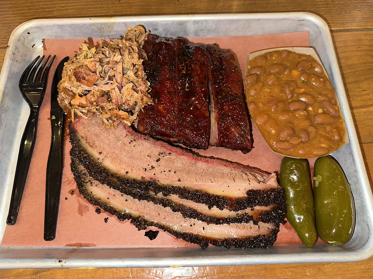A loaded plate of central-Texas BBQ — sliced brisket with a thick smoke ring, glistening pork ribs, pulled pork, beans and pickled jalape&ntilde;os from Pinkerton&rsquo;s in San Antonio.